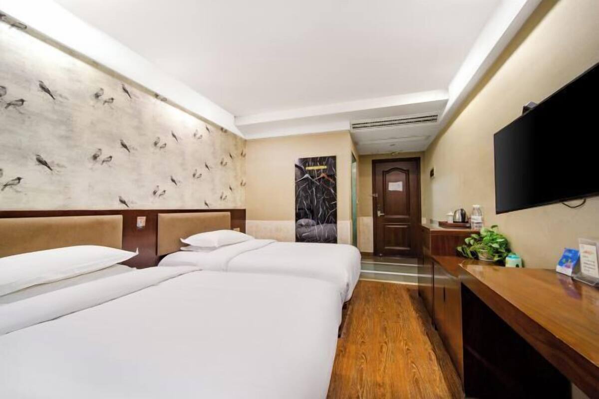 A hotel room with two beds, a wooden desk, a flat-screen TV, and a wall with a bird pattern.