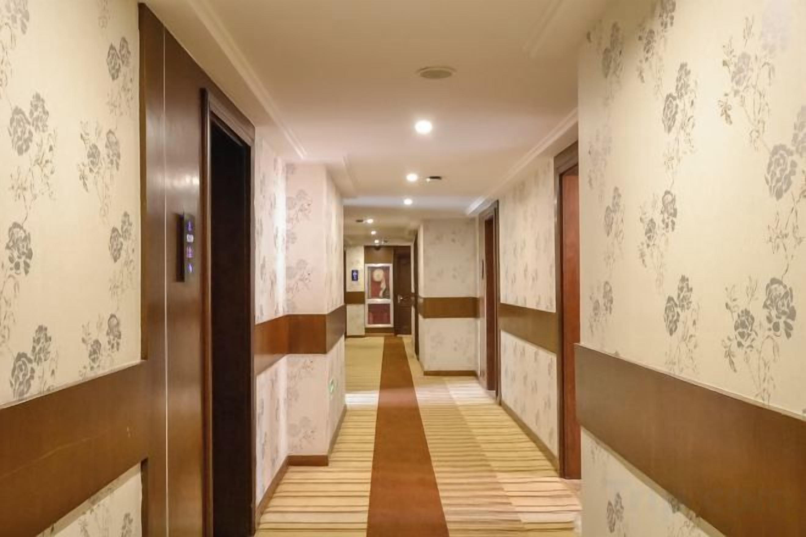 Un pasillo de hotel con papel tapiz estampado, piso alfombrado y puertas que dan a las habitaciones.