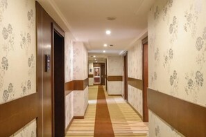 A hotel corridor with patterned wallpaper, a carpeted floor, and doors leading to rooms. - NOMC Hotel (Xianju)