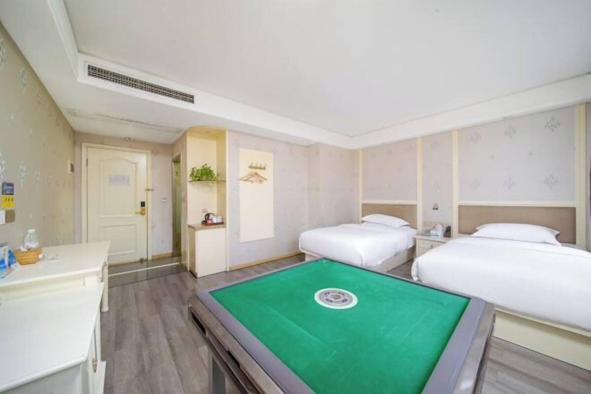 A hotel room with a pool table, two beds, a desk, and a small kitchenette.