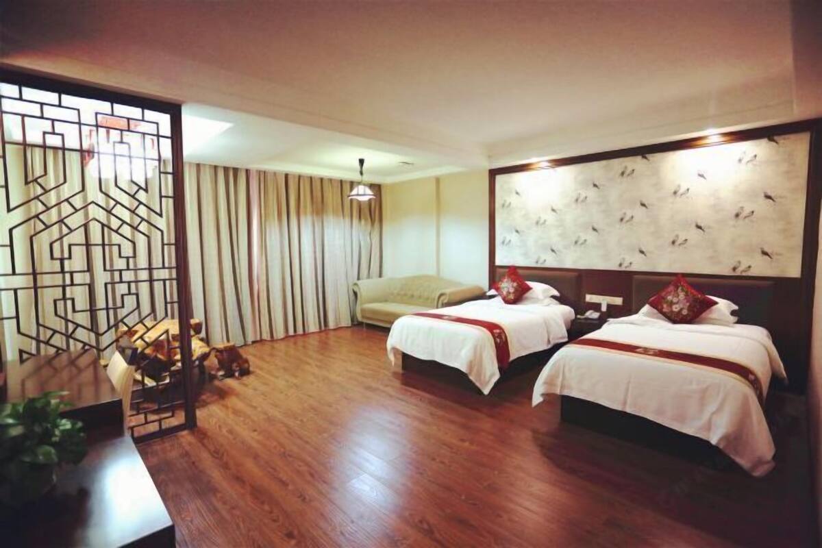A hotel room with two beds, a sofa, a dining table, and a decorative screen.