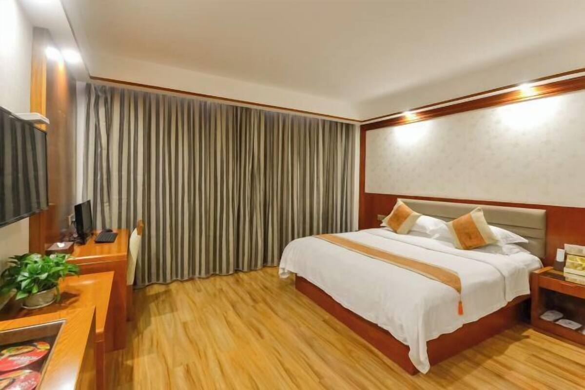 A hotel room with a bed, wooden floor, curtains, a desk with a computer, and a television.