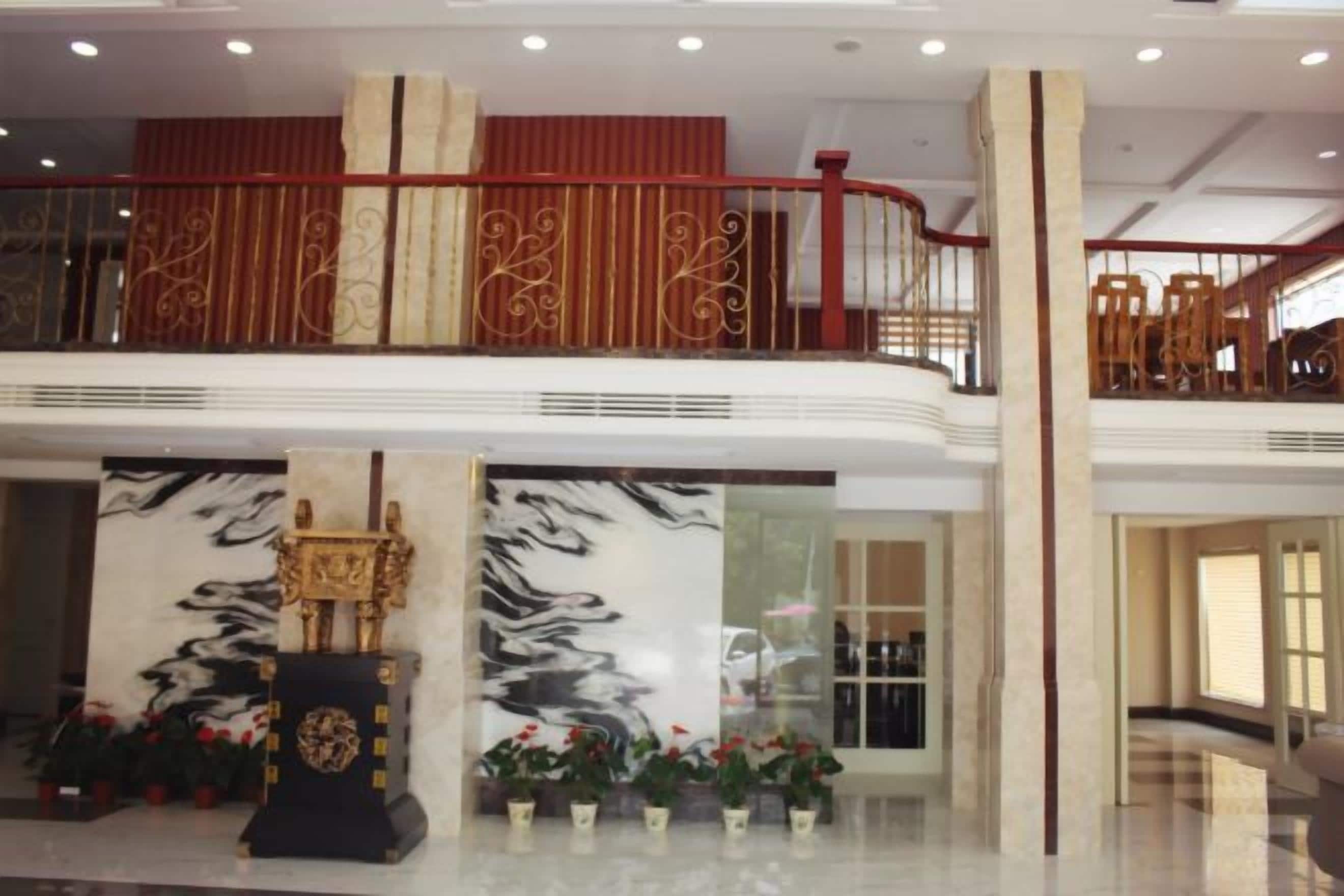 A hotel lobby with a marble reception desk, a large wall mural, and a red railing on the upper level.