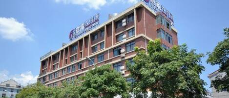 A multi-story hotel with a prominent sign, several windows, and trees in front.