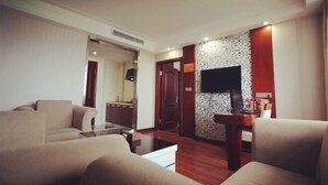 A modern hotel room with a sofa, a coffee table, a TV mounted on the wall, and a small side table with items on it. - NOMC Hotel (Xianju)