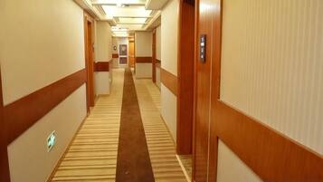 A hotel corridor with carpeted floors, wooden doors, and a central carpeted walkway.