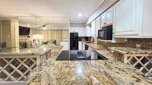 A modern kitchen with granite countertops, white cabinetry, a black refrigerator, and a microwave. - Farr Shores Lakeview Retreat (Hot Springs, AR)