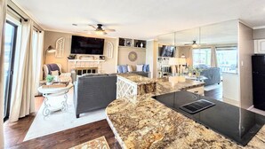 A modern living room with a fireplace, a large TV, and a kitchen area with a granite countertop. - Farr Shores Lakeview Retreat (Hot Springs, AR)