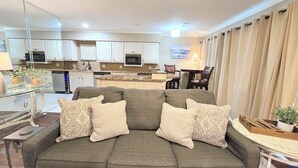 A living room with a grey sofa, patterned cushions, a glass coffee table, and a kitchen in the background. - Farr Shores Lakeview Retreat (Hot Springs, AR)
