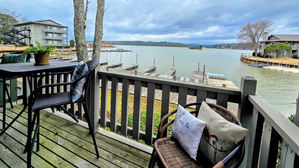 A wooden deck with a view of a lake, docked boats, and buildings in the background. - Farr Shores Lakeview Retreat (Hot Springs, AR)