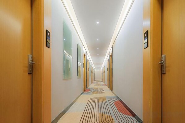 Corredor de hotel com portas em ambos os lados, carpete estampado e iluminação no teto.