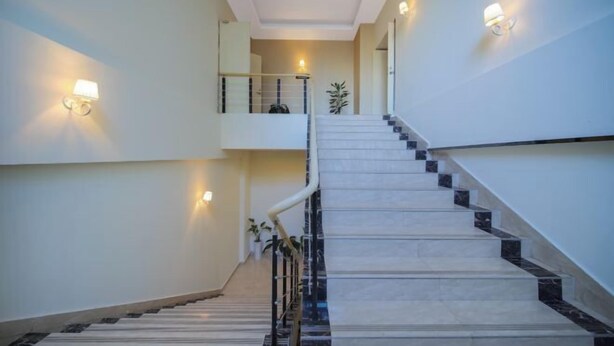 A modern staircase with a handrail, light fixtures on the walls, and a plant on the landing. - Shankee Hotel (Nanjing South Railway Station Shuanglong Avenue Subway Station) (Nanjing)