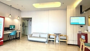 A modern hotel lobby with a reception desk, a sofa, two chairs, a small table, and a TV screen. - Shankee Hotel (Nanjing South Railway Station Shuanglong Avenue Subway Station) (Nanjing)