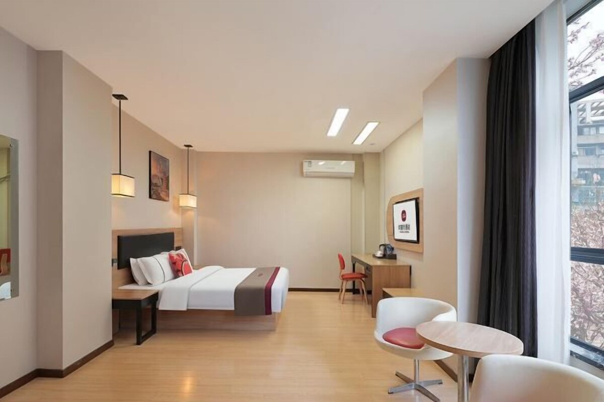 A hotel room with a bed, desk, chairs, and a large window.