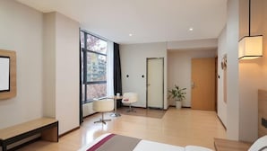 A modern hotel room with a bed, a desk, a chair, a large window, and a door leading to another room. - Shankee Hotel (Nanjing South Railway Station Shuanglong Avenue Subway Station) (Nanjing)