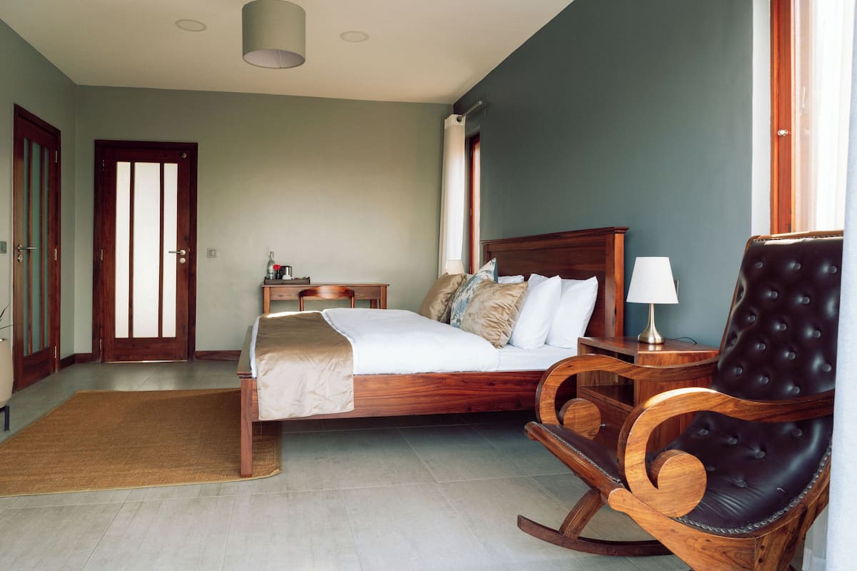 A bedroom with a bed, a wooden rocking chair, a nightstand, and a desk.