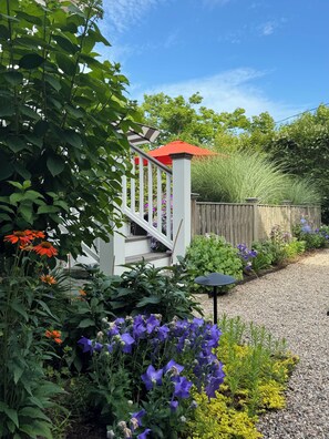 A garden with a wooden fence, a white staircase with a red roof, and various plants and flowers.