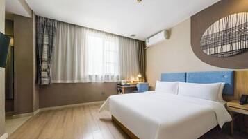 Quarto de hotel com uma cama grande, uma escrivaninha com cadeira, televisão e ar condicionado fixado na parede.
