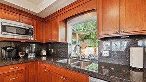 A kitchen with wooden cabinets, a stainless steel microwave, a coffee maker, and a sink with a window view.