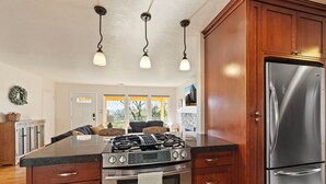 A kitchen with a gas stove, oven, and stainless steel refrigerator. There are wooden cabinets, a marble countertop, and pendant lights.