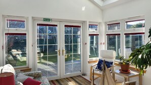 A sunlit room with a skylight, large glass doors leading to a garden, a sofa with cushions, a small table with a potted plant, and a chair. - Escape to a cosy coastal retreat in Montrose, where you can unwind in style. (Montrose)