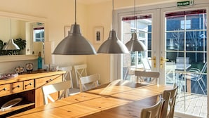 A dining area with a wooden table, white chairs, pendant lights, and a view of the outside through a glass door. - Escape to a cosy coastal retreat in Montrose, where you can unwind in style. (Montrose)