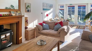 A cozy living room with a sofa, a coffee table, and a fireplace. There is a large window with a view of the outside. - Escape to a cosy coastal retreat in Montrose, where you can unwind in style. (Montrose)