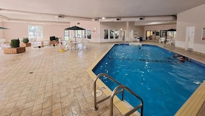 Una piscina interior amb terra de rajola, una escala de piscina i algunes persones nedant.