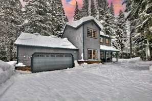 Set amidst snow-covered trees, this two-story house offers a secluded retreat with a garage and sloping roof.