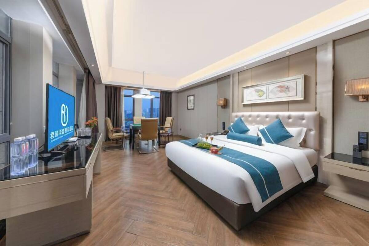 A hotel room with a bed, a desk, a chair, a television, and a dining area.