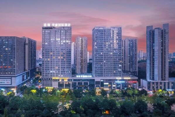 A cityscape with high-rise buildings, one with illuminated signage, and a building with a prominent entrance. - Junrui Huasheng International Hotel (Zhuzhou)