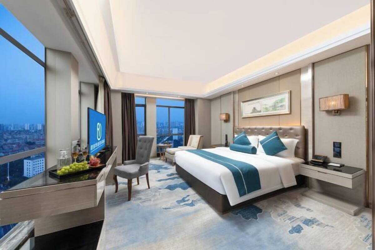 A hotel room with a bed, a desk with a computer, a chair, a TV, and a city view.