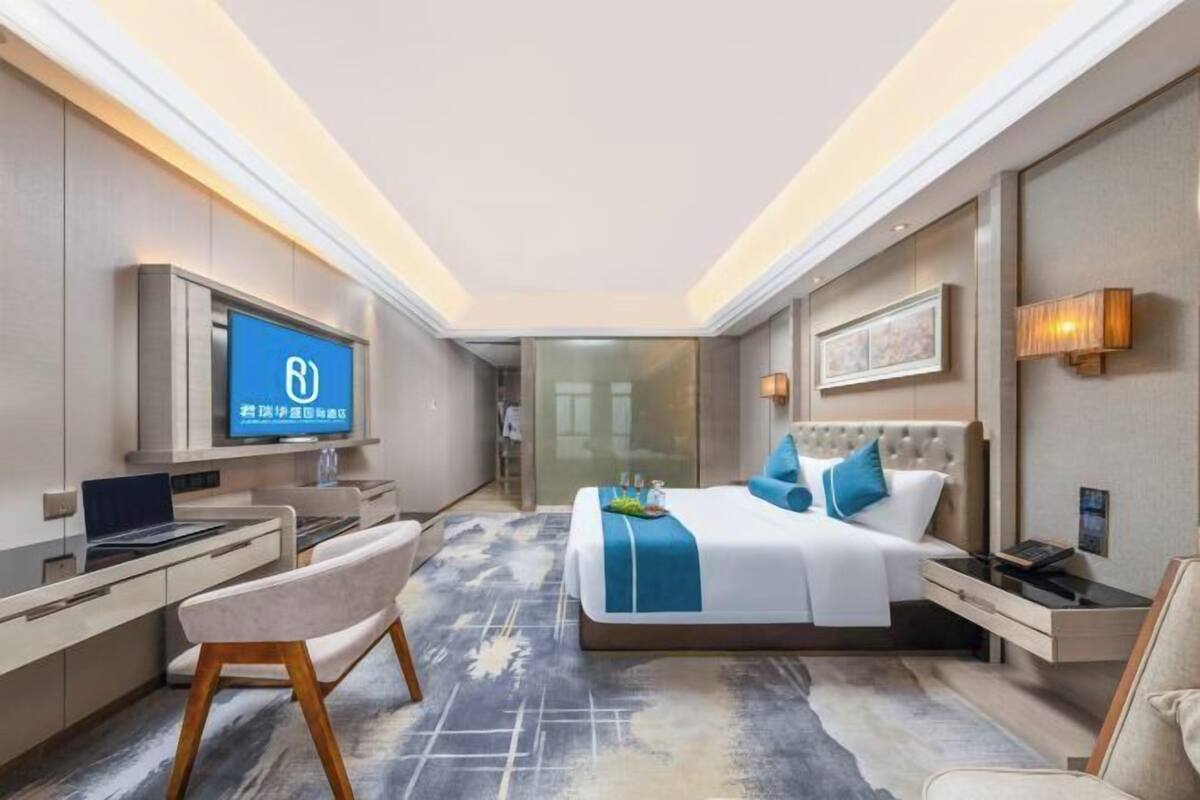 A modern hotel room with a bed, desk, chair, TV, and bedside table.