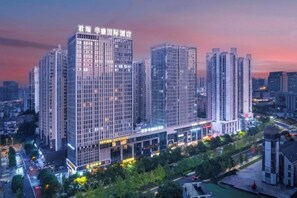 A high-rise building with multiple floors, likely a hotel or office building, with a well-lit facade and surrounded by greenery. - Junrui Huasheng International Hotel (Zhuzhou)