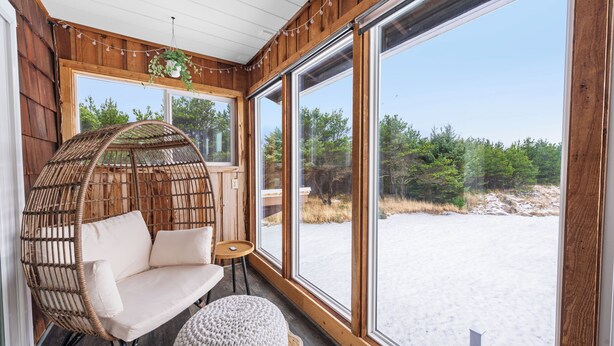 A cozy room with large windows, a wicker chair, a small table, and a round ottoman. - Sunset Shores - Ocean Front Family Retreat HOT TUB  (Ocean Park)