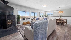 A modern living room with a fireplace, large windows, a sofa, and a dining area. - Sunset Shores - Ocean Front Family Retreat HOT TUB  (Ocean Park)