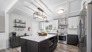 A modern kitchen with dark wood cabinets, a central island, stainless steel appliances, and a white marble countertop. - Sunset Shores - Ocean Front Family Retreat HOT TUB  (Ocean Park)
