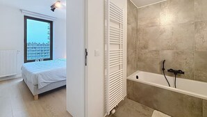 Une chambre à coucher avec un lit, une fenêtre donnant sur un beau paysage, et une salle de bain équipée d’une baignoire et d’une douche.