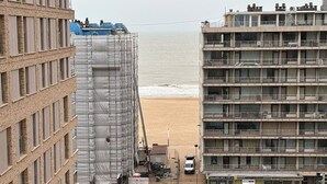 Un bâtiment situé sur la côte, avec vue sur la plage, un chantier de construction sur la gauche et un immeuble à plusieurs étages sur la droite.