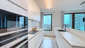 Une cuisine moderne avec des meubles blancs, un four encastré et une grande fenêtre donnant sur la ville.