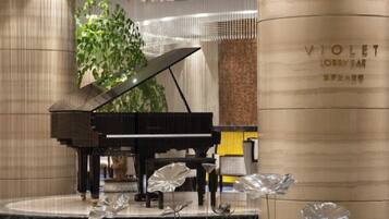 Un piano de cola en un escenario, con una columna que dice 'VIOLET LOBBY BAR' al fondo.