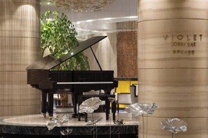 Un piano de cola en un escenario, con una columna que dice 'VIOLET LOBBY BAR' al fondo.