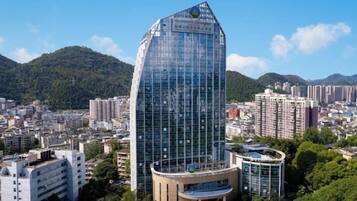Un moderno edificio de cristal con techo curvo, rodeado de edificios urbanos y zonas verdes.