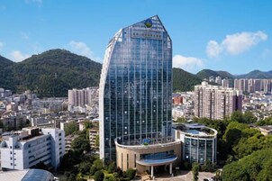 Un moderno edificio de cristal con techo curvo, rodeado de edificios urbanos y zonas verdes.