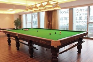 Una mesa de billar en una habitación con ventanas amplias y una planta.