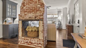 Un salón amplio con chimenea de ladrillo, suelo de madera y un gran ventanal que proporciona luz natural.