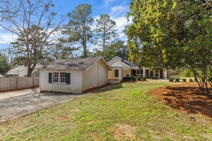 A single-story house with a front porch, a fenced yard, and a large tree to the right. - Bellwood Beauty (Northport)