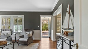 Una habitación con mobiliario de mimbre, un tapete blanco y un modelo de velero sobre una consola.