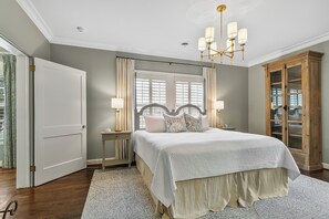 A bedroom with a large bed, a chandelier, a wardrobe, and a window with curtains. - Bellwood Beauty (Northport)
