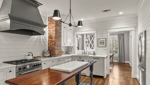 Una cocina con armarios blancos, una isla de madera, una pared de acento de ladrillo y una lámpara colgante moderna.
